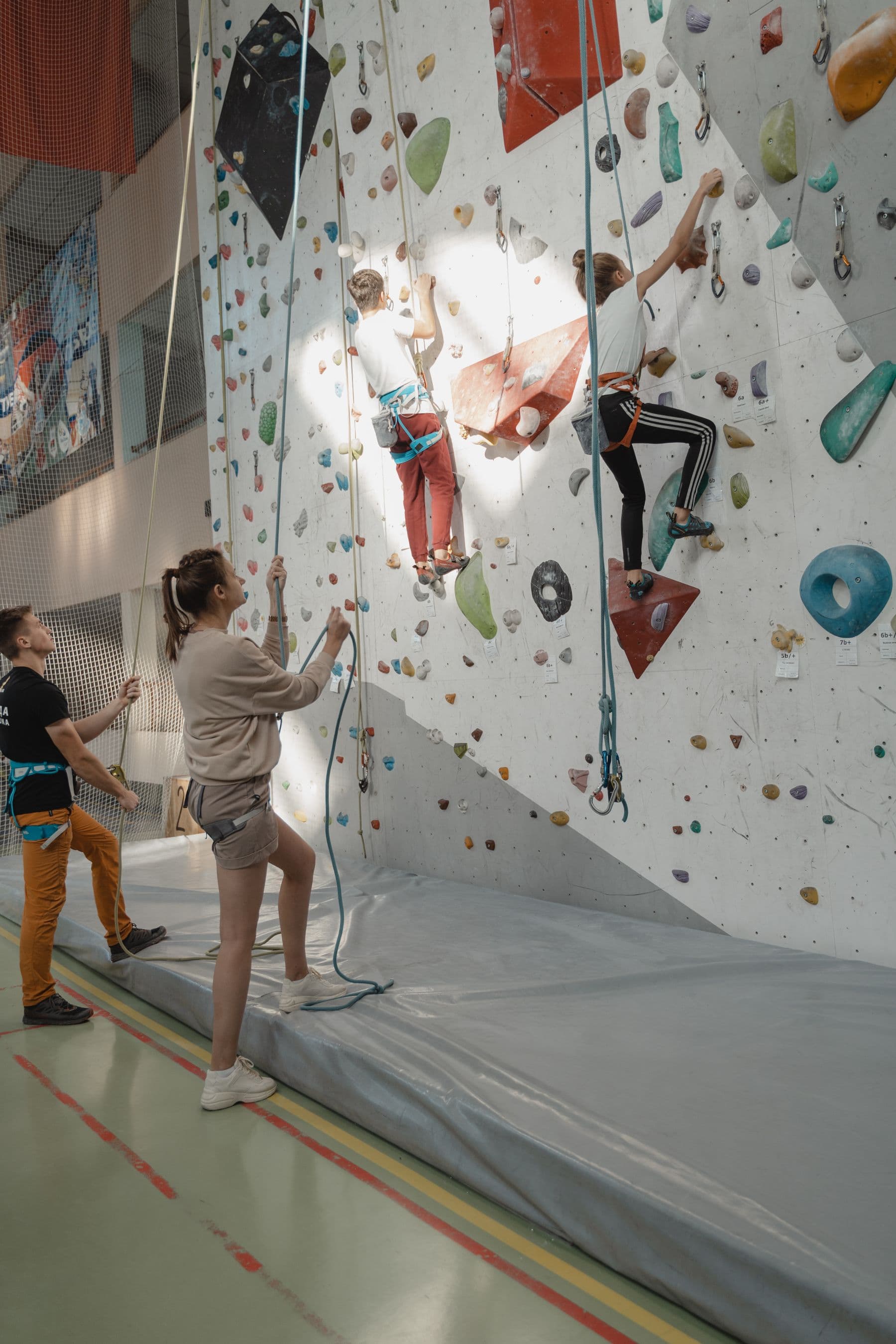 Un éducateur sportif accompagne des enfants sur un mur d'escalade.